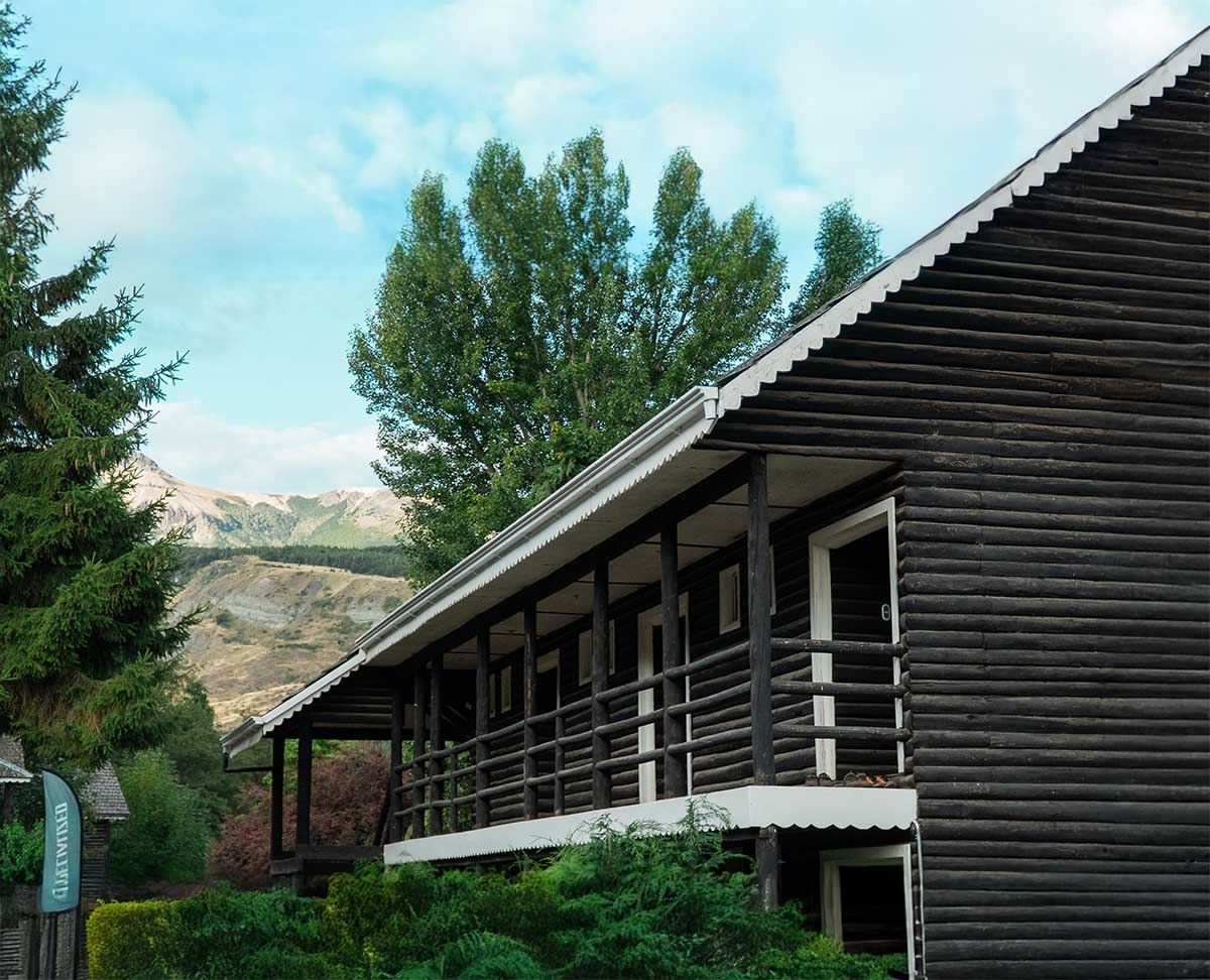 Cabaña de madera oscura del Patagonia Bikers Lodge, rodeada de árboles y montañas